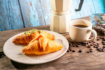 croissant in white plate, coffee beans, and coffee kettle on old wooden table.soft focus.