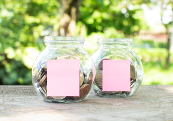 On a wooden table, there are glass jars with coins and attached blank stickers for inscriptions. Investment budget.