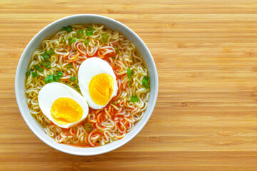 Instant noodles with boiled egg and spring onion in a bowl on a bamboo chopping board.