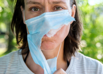 Portrait of an unhappy, tired woman in a torn medical mask. Concept of defeating the virus and...