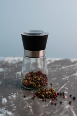 Glass pepper mill with a mixture of peppercorns on a dark background, vertical format and copy...
