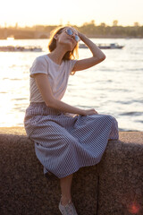 slender woman with short hair sits by the river at sunset