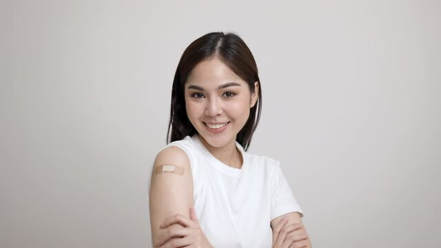 Vaccination. Young beautiful asian woman getting a vaccine protection the coronavirus. Smiling happy female showing arm with bandage after receiving vaccination. On isolated white background.