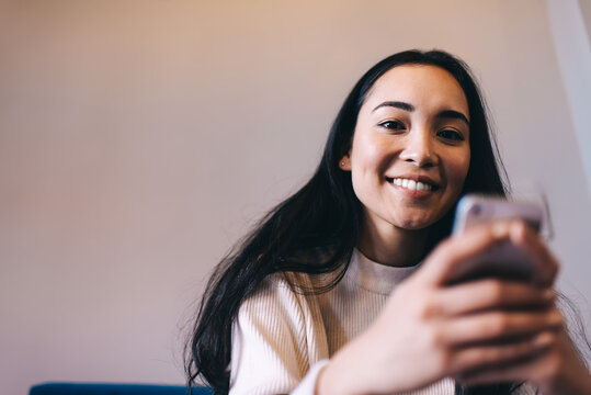 Portrait of cheerful hipster girl smiling at camera while using smartphone gadget for online communication and social networking, prosperous teenager connecting to 4g on cellphone technology
