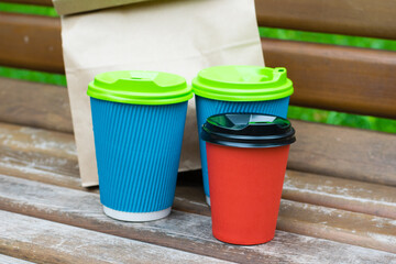 Paper bag with takeaway food and glasses with coffee on a bench in the park. Concept of food delivery, communication during quarantine covid 19