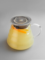 Teapot of ginger tea with a wedge of orange on gray background