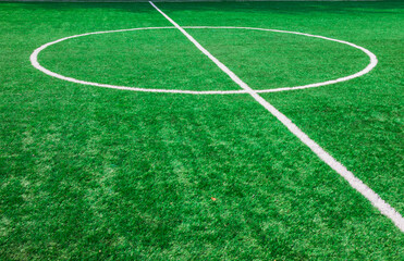 Fototapeta premium The centre of soccer field with artificial green grass and white lines near the school. Amateur football field. Sunny summer day