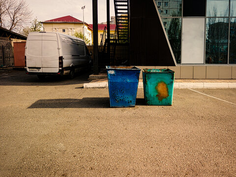 Trash Dumpsters Rusty. Dustbins Full Of Litter Near Office Building With New Commercial Van On Background