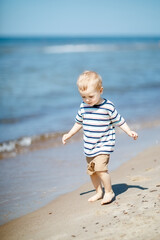 One little beautiful kid walking along the seashore at the day time.