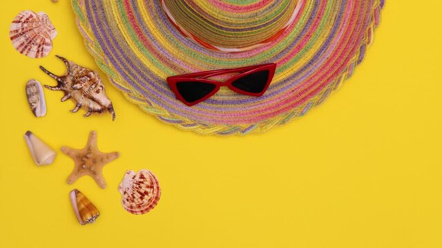 Red sunglasses, a striped sun hat, and seashells appear on a yellow background. Summer and vacation concept. Stop motion animation. Copy space.