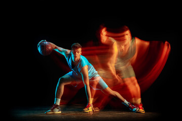 Professional male basketball player in blue uniform playing basketball isolated over dark studio...