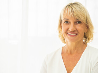 Portrait of beautiful middle-aged woman smiling friendly and looking in camera in the living room. Realistic images without retouching with their imperfections..