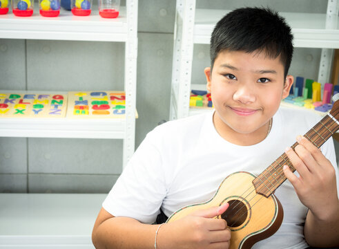 Portrait Of Disabled Child In A Wheelchair Is Playing The Ukulele In Sensory Activity. Concept Disabled Child Learning In School.