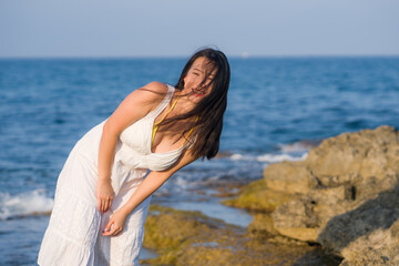 summer lifestyle portrait of young beautiful and happy Asian woman at the beach - Attractive Korean girl by the sea enjoying holidays trip on rock cliff with ocean view
