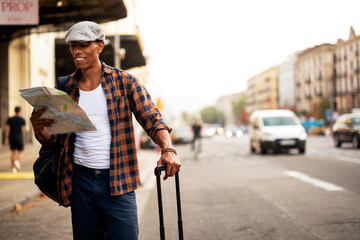 Happy young man with a city map. Young handsome male traveler, standing on the street and looking at the map...