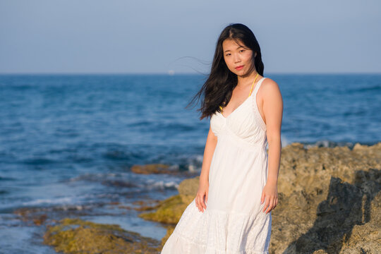 summer lifestyle portrait of young beautiful and happy Asian woman at the beach - Attractive Korean girl by the sea enjoying holidays trip on rock cliff with ocean view