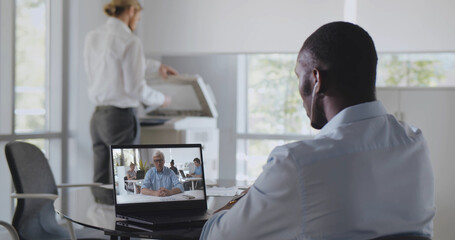 Back view of african employee sitting at desk in office having video chat with boss on laptop