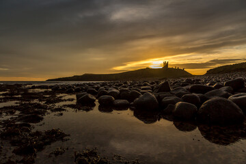 Fototapeta na wymiar The most beautiful sunrise at Dunstanburgh Castle with the famous slippery black boulders in Northumberland, as the sky erupted with colour