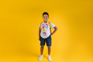 Fototapeta na wymiar Happy boy wearing hawaiian lei flower necklace with backpack on yellow background