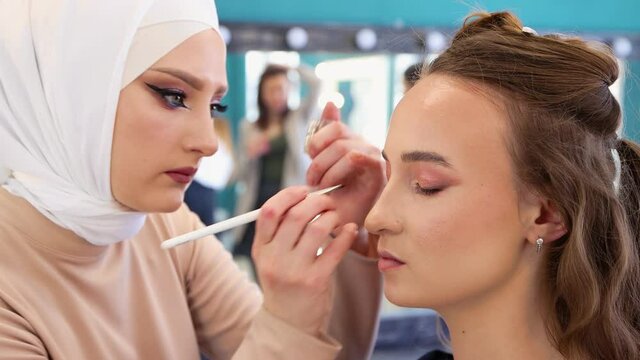 The girl master with a brush applies gentle shadow to the eyelid close-up. Makeup artist makes makeup to a young woman. Beautician, business concept. Beauty salon, skin care. UHD 4K.