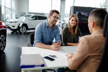 Female car seller sitting in car salon with a customers and discussing about car performances.