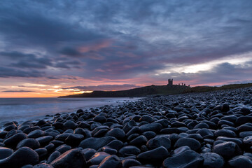The most beautiful sunrise at Dunstanburgh Castle with the famous slippery black boulders in...