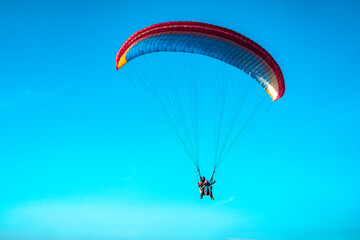 Doubles paragliding against a clear blue sky. A multi-colored papaplan flies in the clear sky closeup.