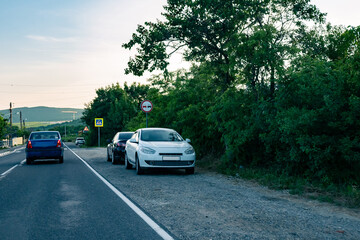 Parked cars on the sidelines on a country road. Cars on the edge of a road in the countryside during the day.