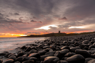 The most beautiful sunrise at Dunstanburgh Castle with the famous slippery black boulders in Northumberland, as the sky erupted with colour