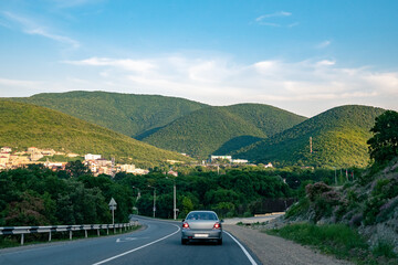 Car rides along the highway among green mountains in sunny weather. Car rides on a road through forest hills.