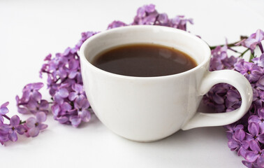 Lilac and cup of coffee in flat style on white wooden background. Beautiful spring. Overhead view. Flat lay, top. Summer season. Natural spring style.
