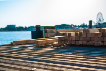 Piled wood on a pier under construction. Tree for building in the sunlight on a background of blue sea. Building a pier in the morning light of the sun.