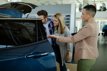 Young saleswoman shows a couple a car at a car dealership. Buying or renting a car.