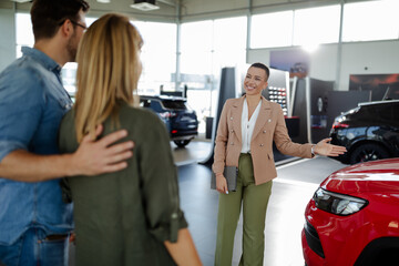 Young saleswoman shows a couple a car at a car dealership. Buying or renting a car.