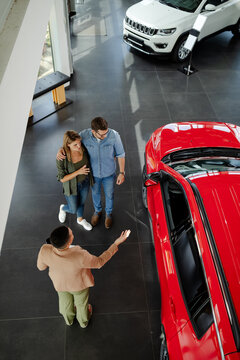 Top view of young couple choosing and trying new car in auto salon.