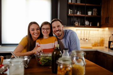 Portrait of happy family making a salad for healthy lunch while looking at camera. Healthy lifestyle