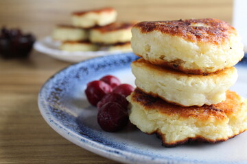 Three pancake cheesecakes lie stack of slides on top of each other on plate table with cherry cherry . View from the side. Breakfast is Russian Ukrainian. Dishes cottage cheese. Place with copyspace