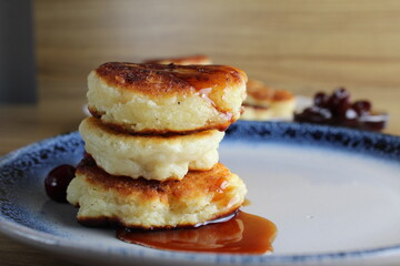 Three pancake cheesecakes lie stack of slides on top of each other on plate table with cherry cherry . View from the side. Breakfast is Russian Ukrainian. Dishes cottage cheese. Place with copyspace