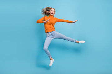 Fototapeta na wymiar Photo of adorable strong young lady wear orange sweater jumping high practicing karate smiling isolated blue color background