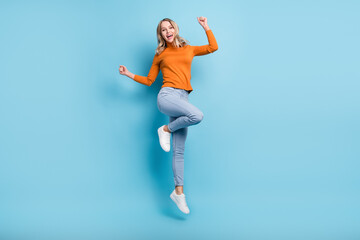 Fototapeta premium Photo of adorable lucky young lady wear orange sweater jumping high rising fists smiling isolated blue color background