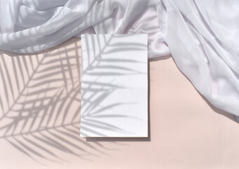 Sunlight tropical stationery flat lay. Mockup empty blank, greeting card or menu with silk fabric on pink background. Palm leaves shadow. Summer wedding minimal concept. Elegant layout. Copyspace.