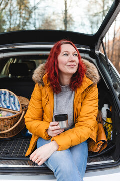 Smiling woman drinking tea in car trunk in park