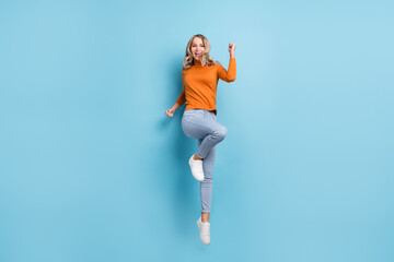Fototapeta na wymiar Photo of lucky sweet young woman dressed orange pullover smiling rising fists isolated blue color background
