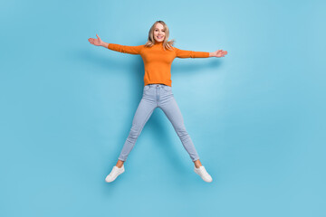 Fototapeta na wymiar Photo of cute adorable young lady wear orange sweater jumping high like star smiling isolated blue color background