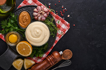 Homemade mayonnaise sauce and ingredients lemon, eggs, olive oil, spices and herbs, black background copy space. Food cooking background. Top view.