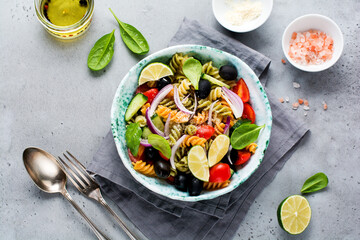 Whole grain pasta with vegetables on a white plate on a light grey slate, stone or concrete background. Top view with copy space.