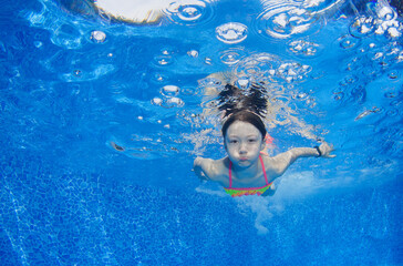 Young girl deftly swim underwater in pool.