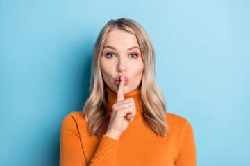 Photo of funny charming young woman dressed orange pullover finger mouth asking shut up isolated blue color background