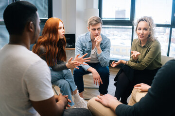Young group of multiethnic business people share ideas during brainstorming on background of window. Happy creative colleagues working together in teamwork discuss project plan in office.