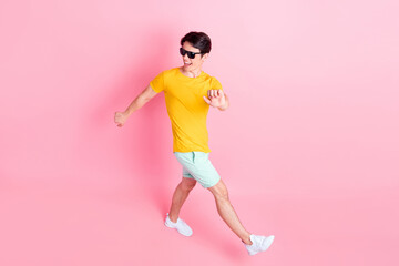 Fototapeta na wymiar Photo of funky pretty young man wear yellow t-shirt dark eyewear smiling walking dancing isolated pink color background